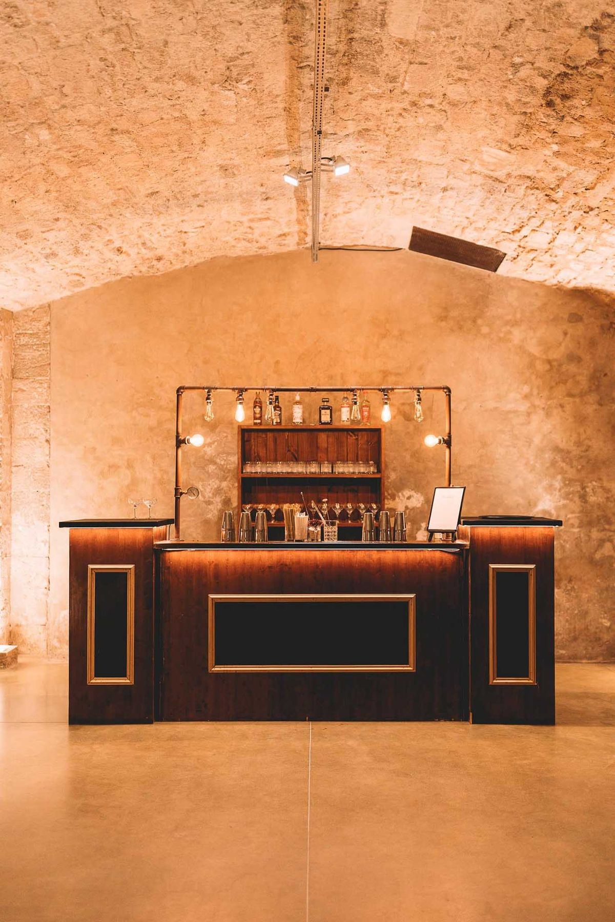 Walnut wood bar with Edison bulb copper pipe frame in vaulted stone cellar