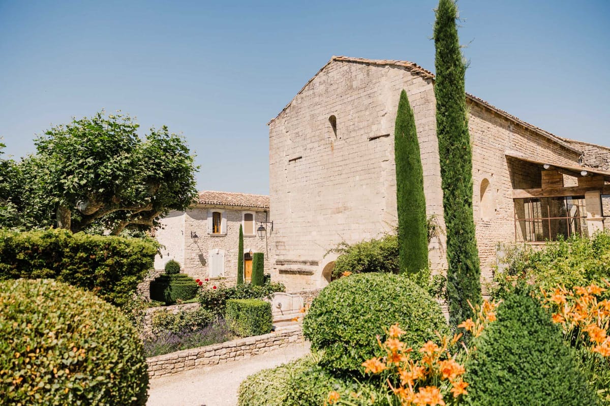 Provencal stone mas with terracotta roofs, clipped boxwood hedges, cypress trees, and lavender borders