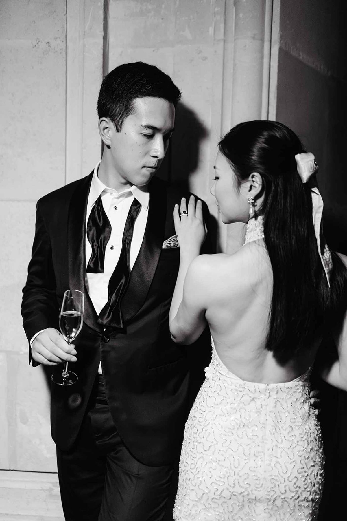 Black-and-white portrait of bride and groom in formal attire sharing an intimate moment with champagne flute