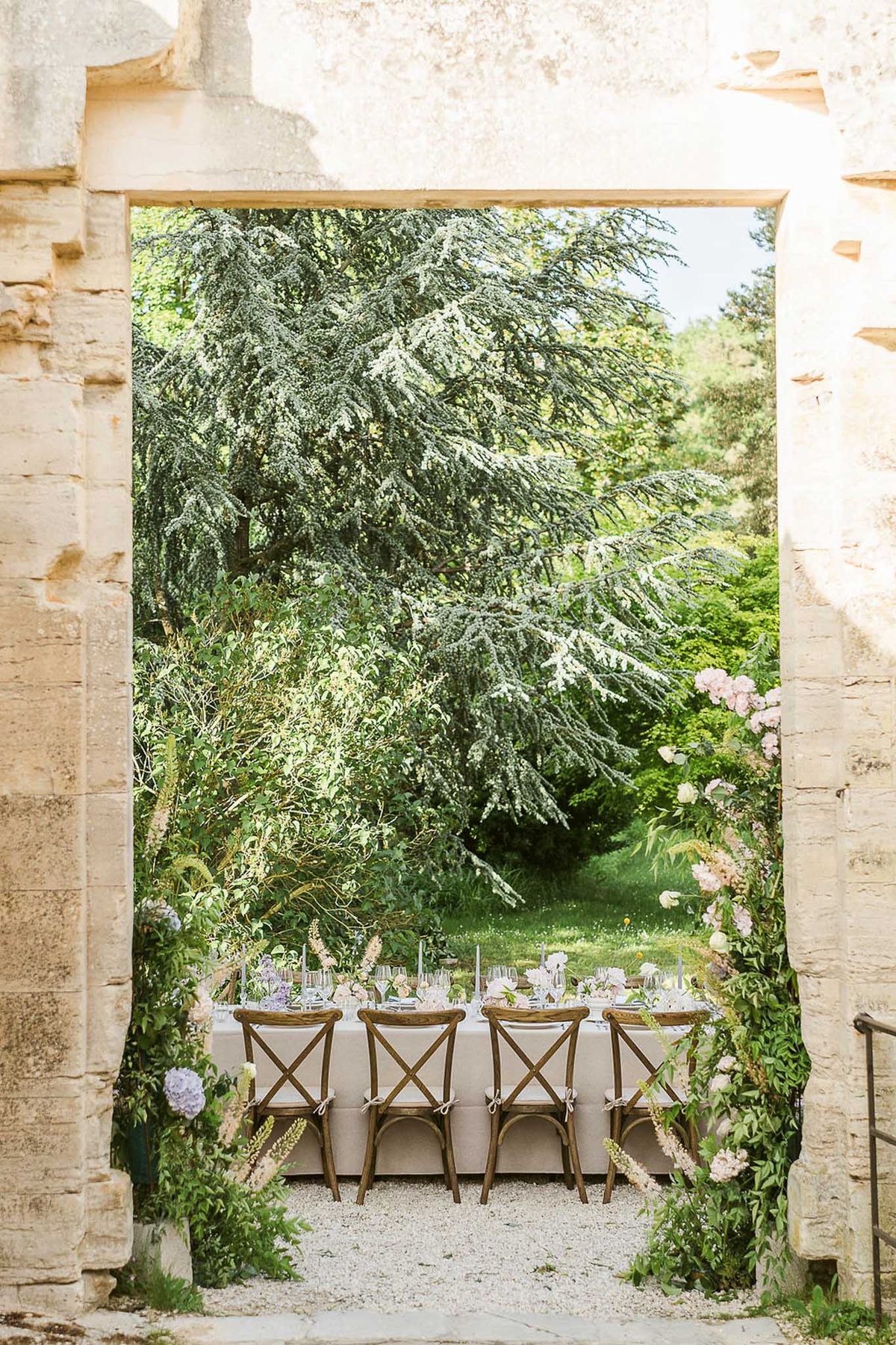 Outdoor reception table framed through a stone archway with hydrangeas and roses at a historic chateau garden