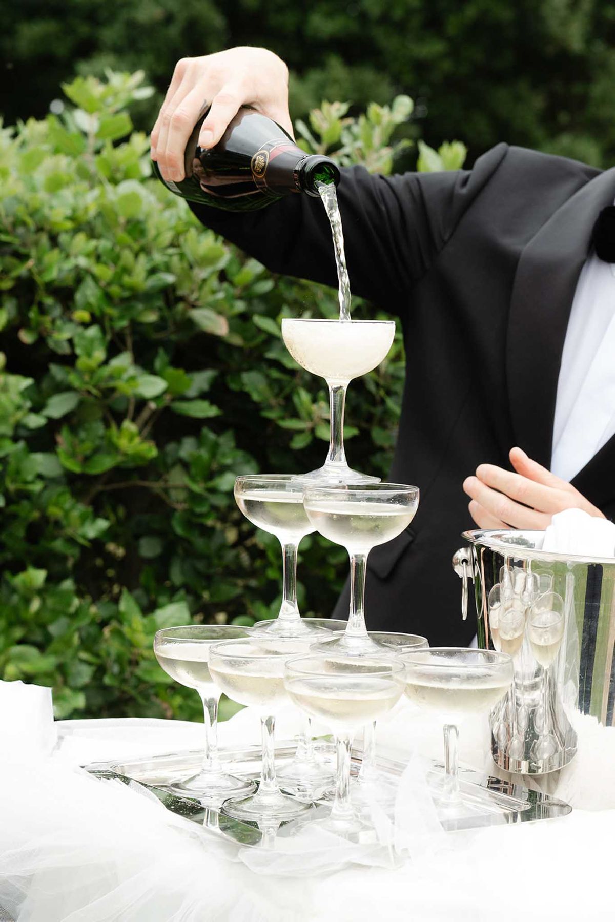 Champagne being poured into a coupe glass tower during an outdoor garden wedding reception