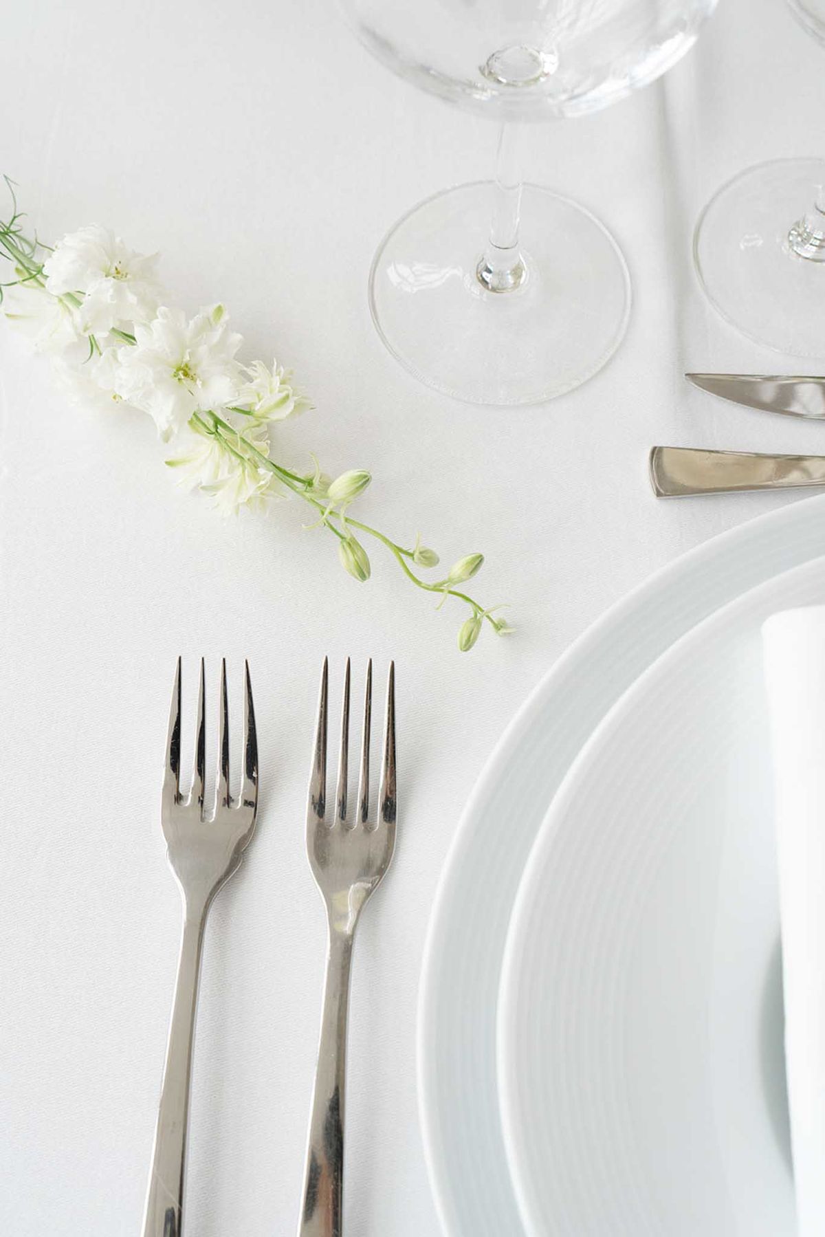 Minimalist table setting flat lay with pale blue and white plates, silver flatware, and single white freesia stem
