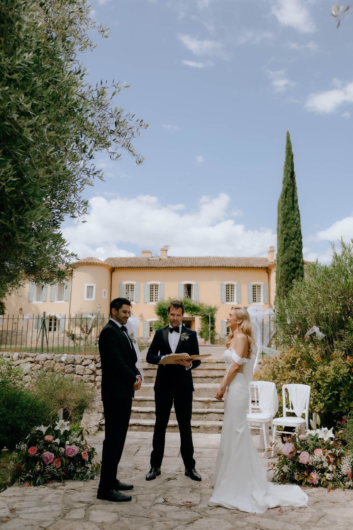 Ceremony before ochre bastide with blue shutters, blush and pink rose ground clusters on stone courtyard