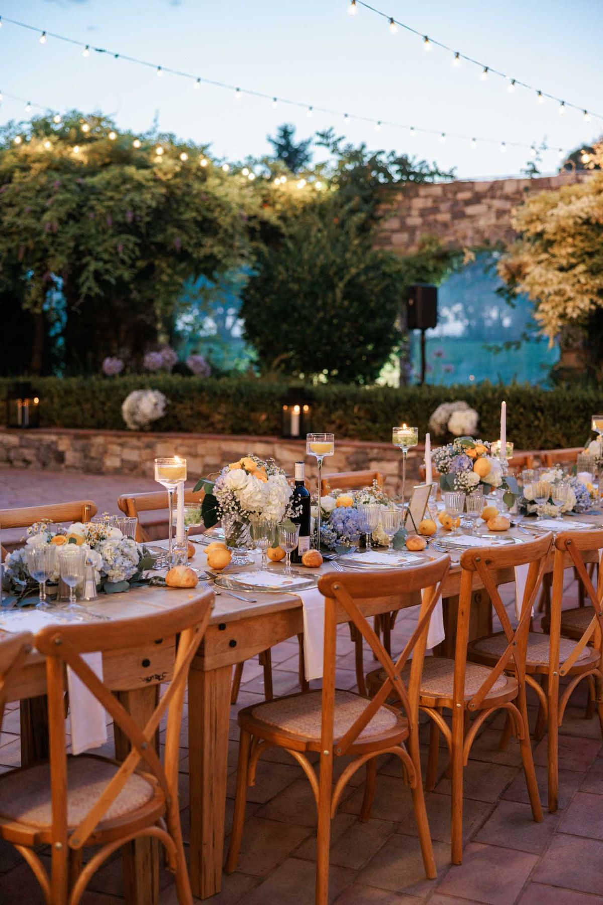 Outdoor reception on terrace at dusk with hydrangea centerpieces, string lights, and garden backdrop