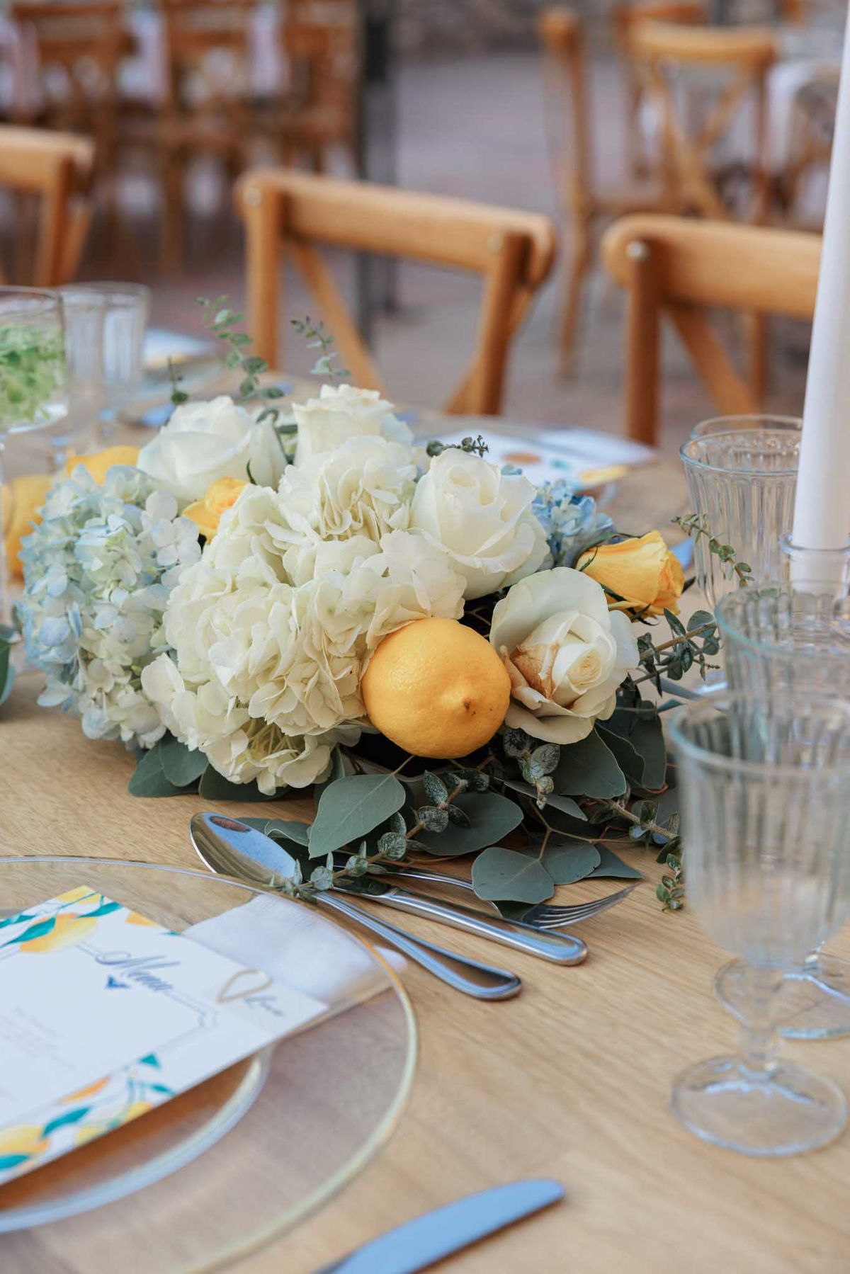 Reception table centerpiece with cream roses, hydrangeas, golden lemons, and eucalyptus on wooden table