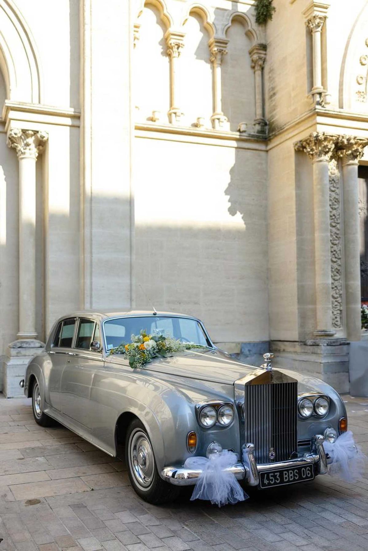 Silver-grey vintage Rolls-Royce with white floral bouquet on hood in neoclassical column courtyard