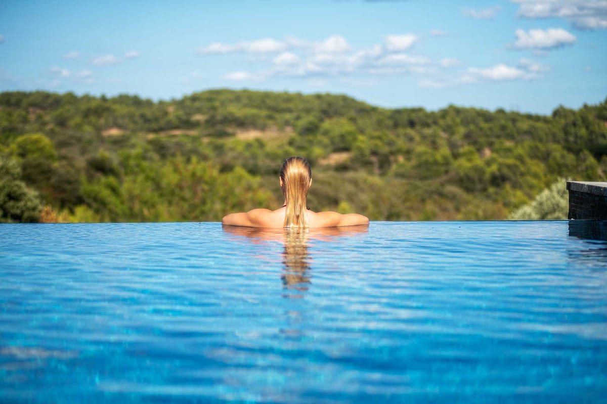 Woman relaxing in an infinity pool overlooking wooded hills at a French chateau property
