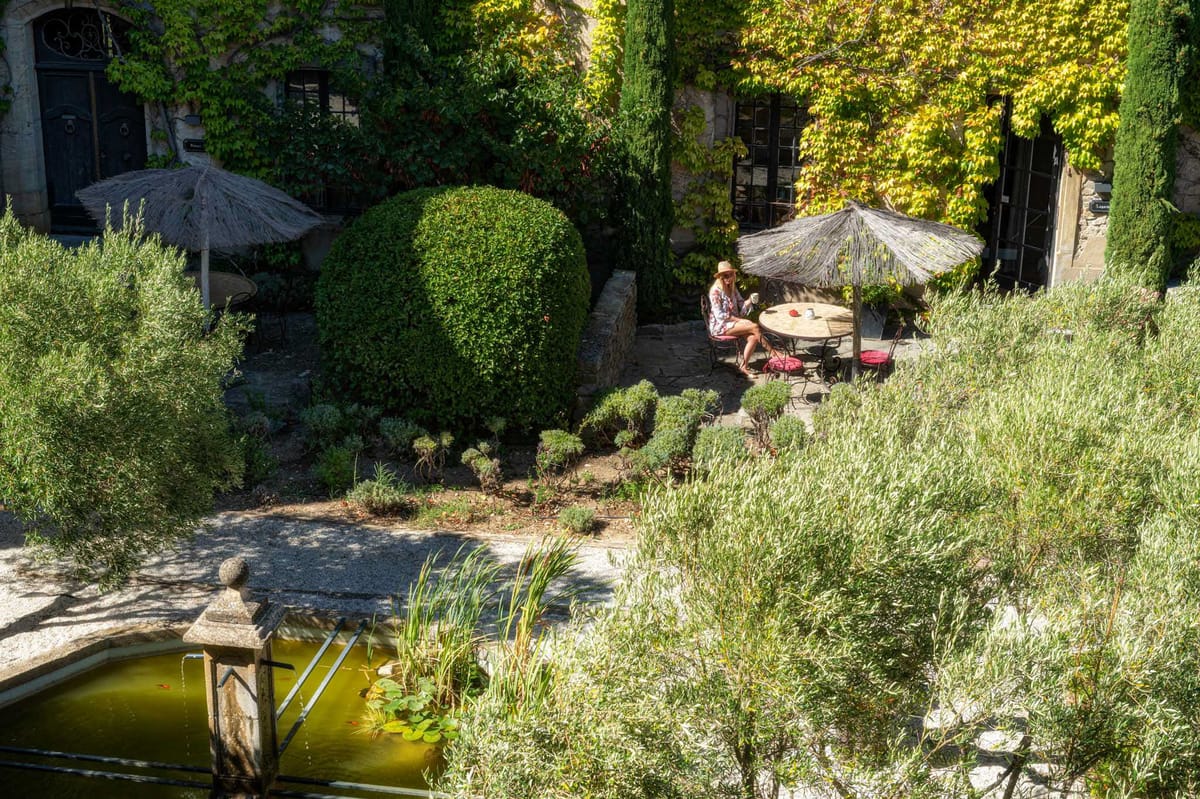 Courtyard garden at a Provencal stone property with thatched parasols, topiary, and vine-covered facade