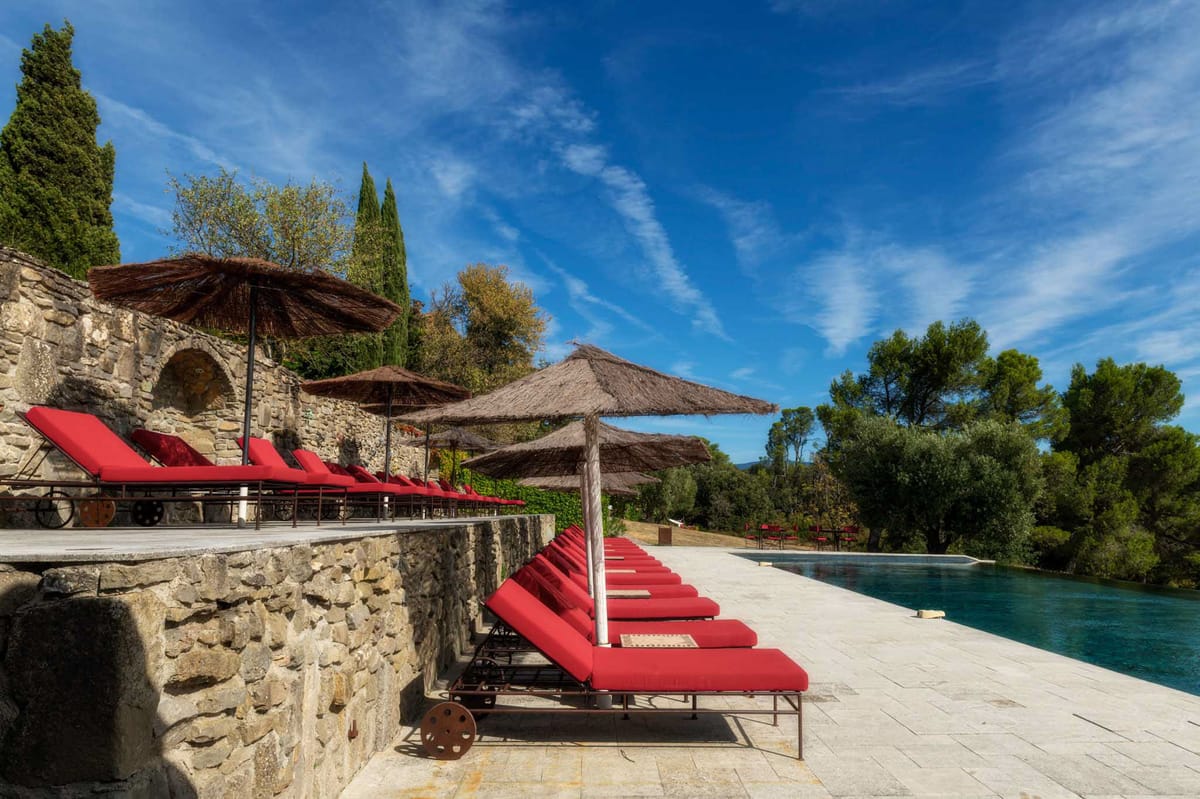 Estate pool terrace with red-cushioned loungers thatched parasols dry-stone wall and calm dark water