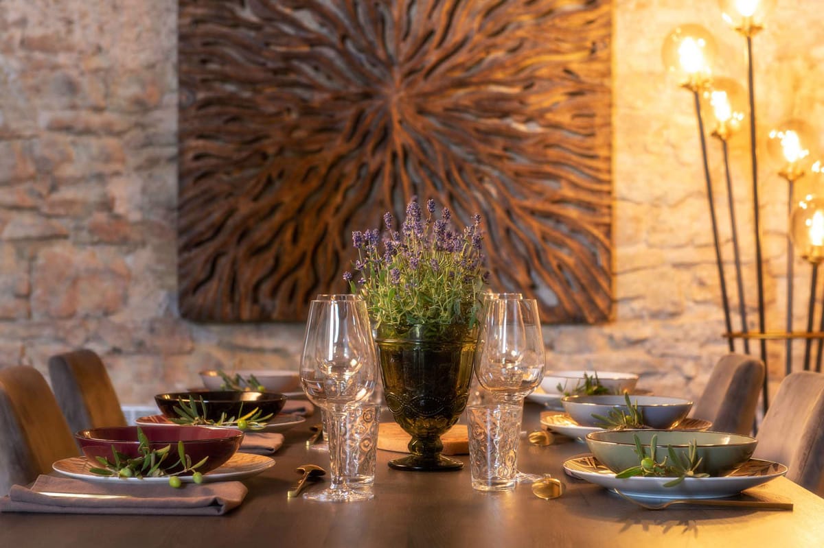 Reception table setting with burgundy and sage bowls, gold cutlery, lavender in olive urn against stone walls