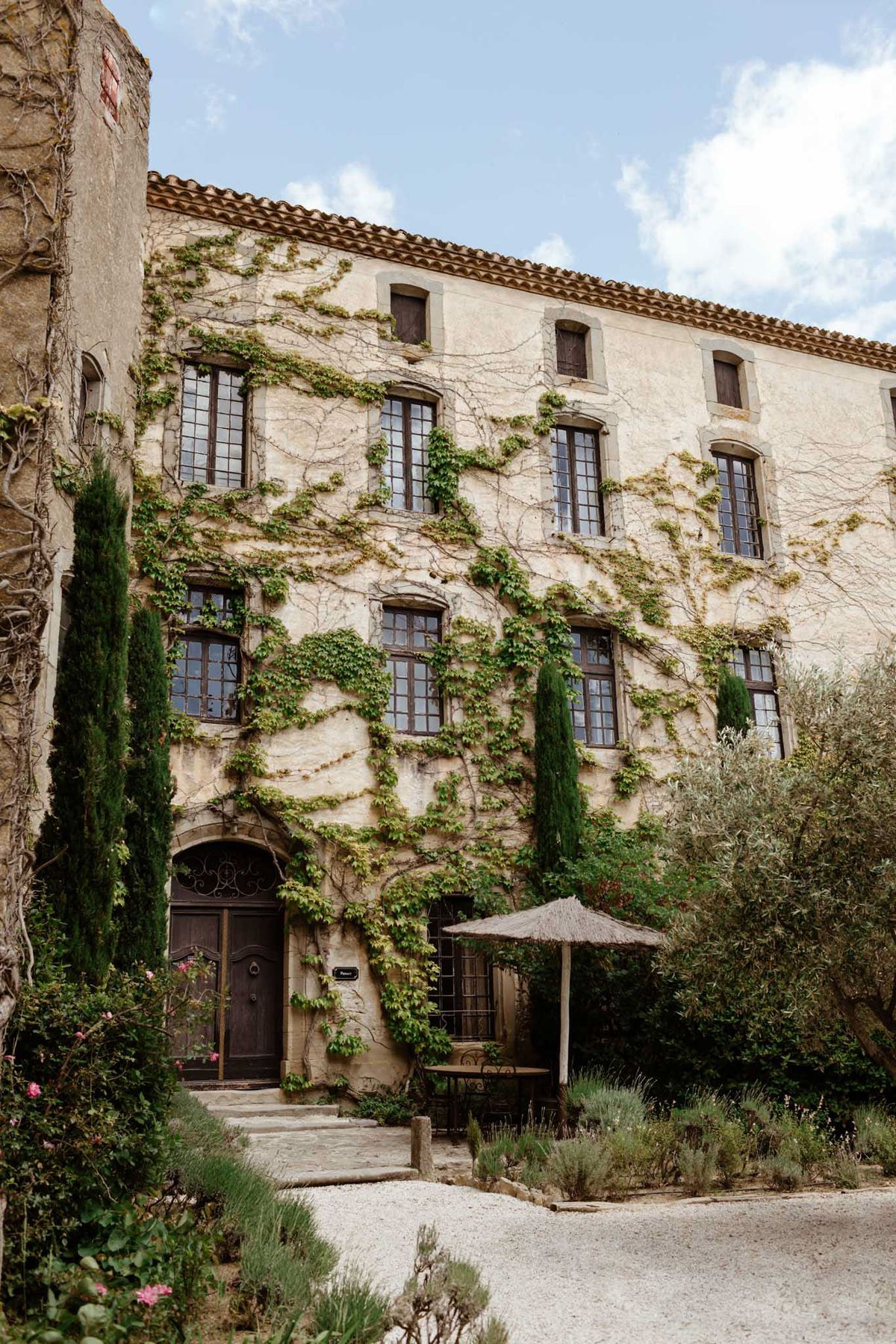 Ivy-covered limestone Provencal chateau with cypress trees lavender and gravel courtyard with wicker parasol