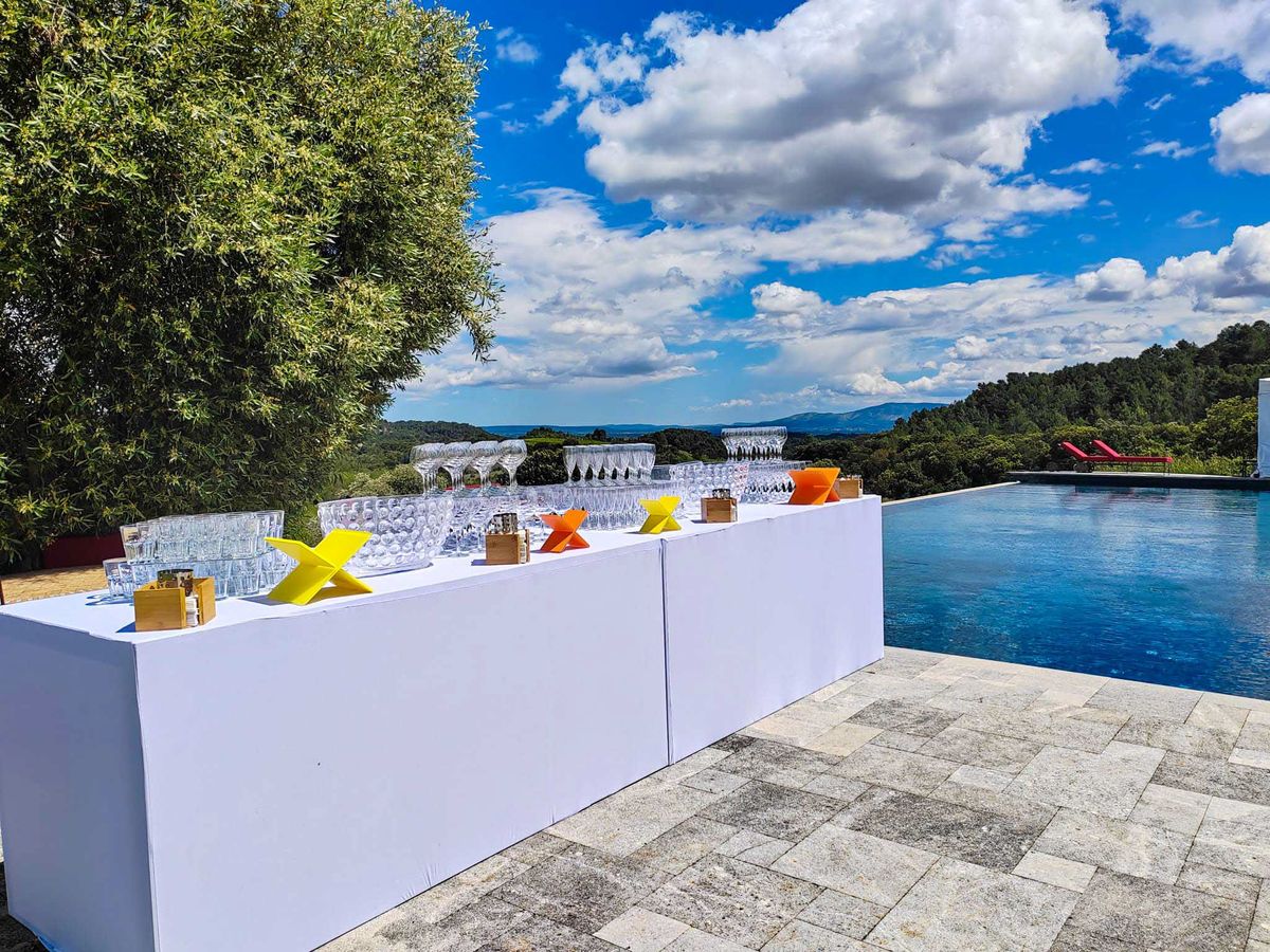 Poolside bar with coupe glasses and yellow geometric accents overlooking forested hills from stone terrace