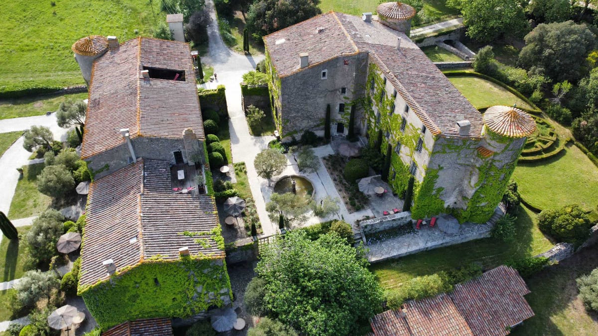 Aerial drone view of French chateau complex with stone buildings, courtyard fountain, boxwood topiaries and formal parterr...