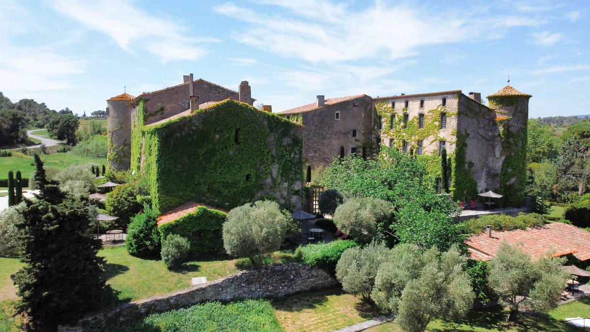 Aerial view of ivy-covered chateau with corner towers, parasol seating, and vineyard backdrop