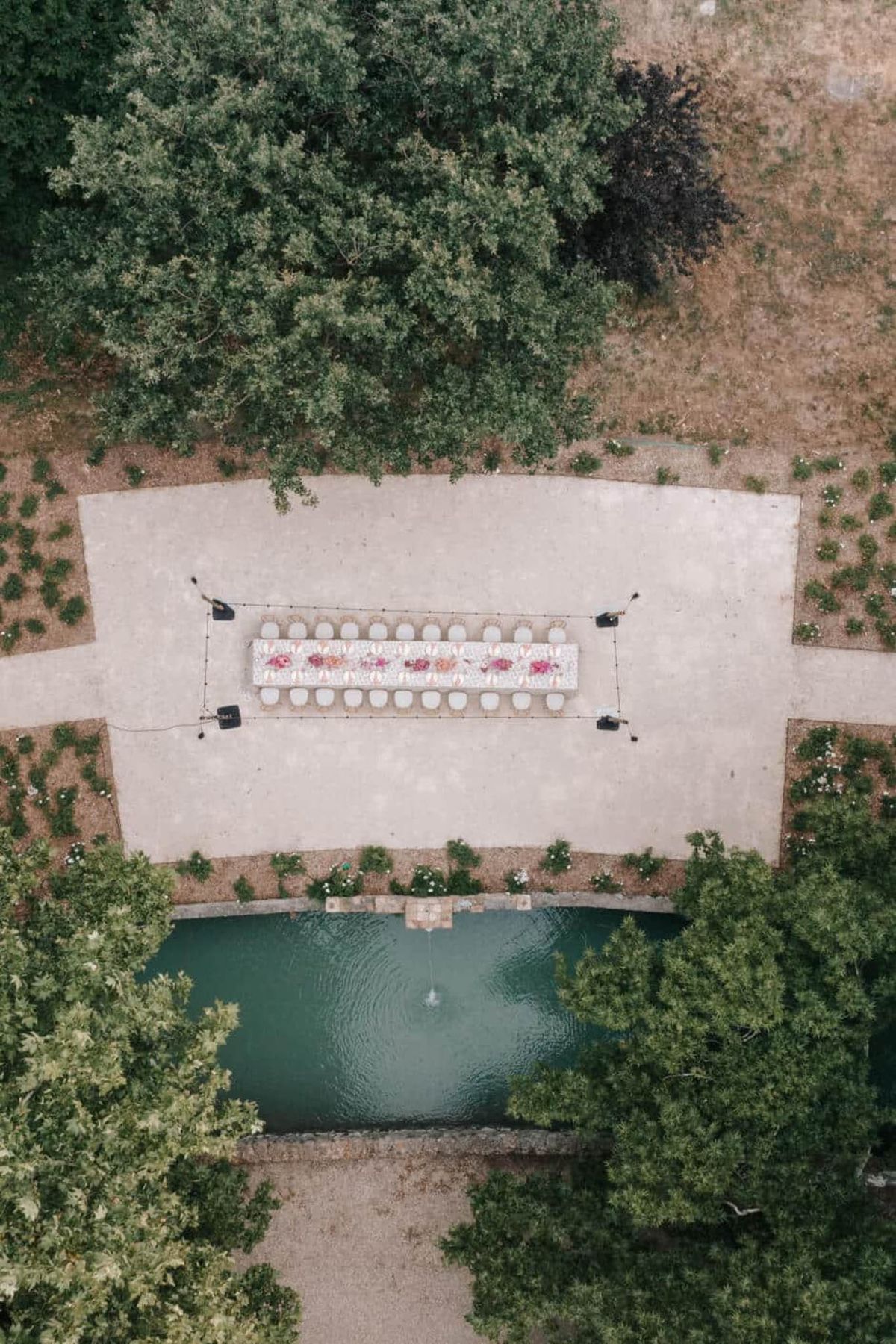 Aerial view of long banquet table with hot pink and coral centerpieces beside ornamental pool