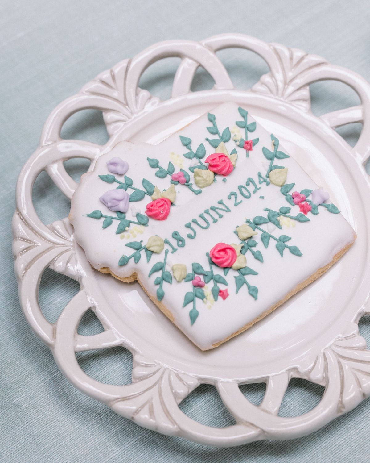 Heart-shaped wedding cookie with floral icing and date on ornate white porcelain plate