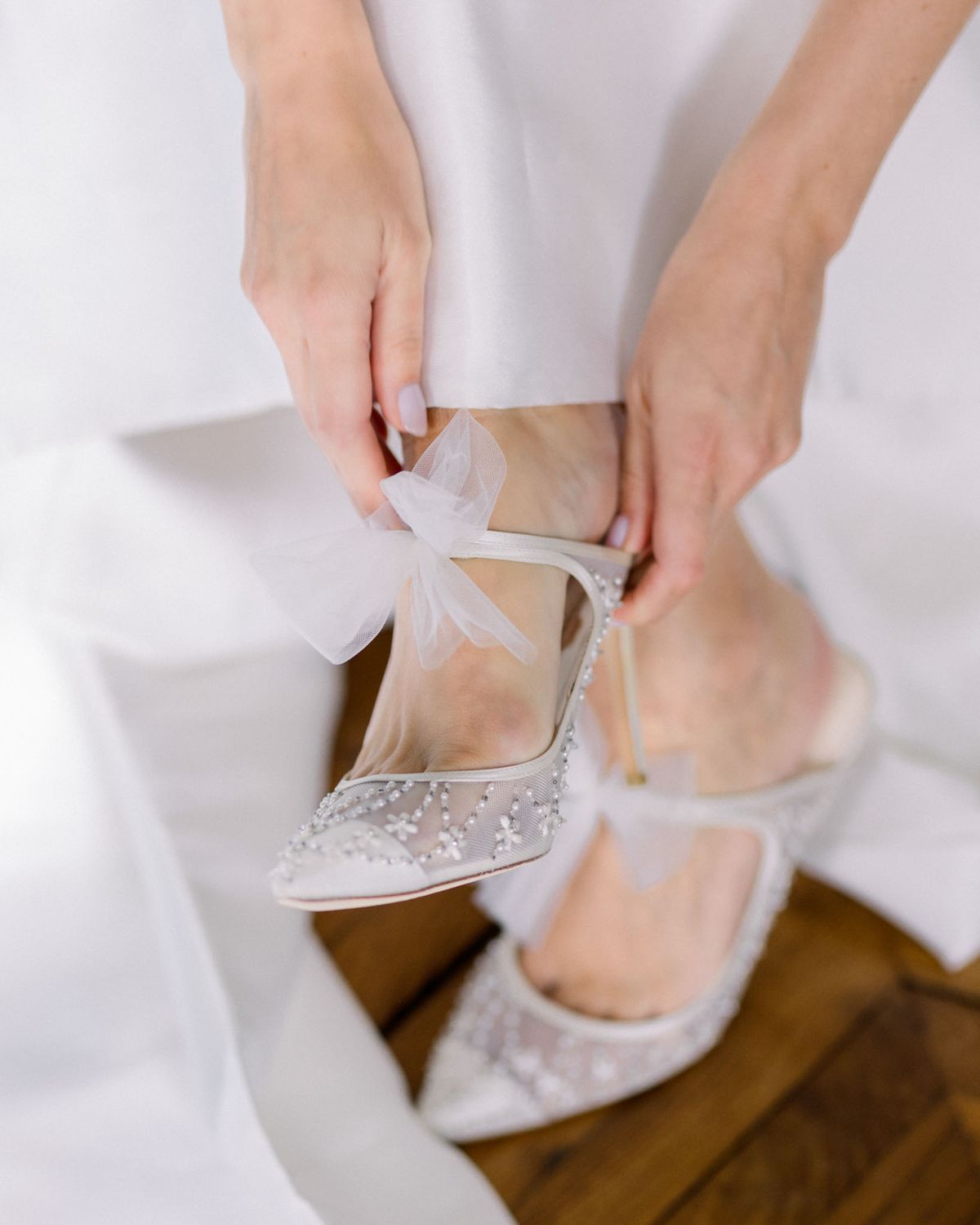 Close-up of bride putting on ivory heels with pearl beading and tulle bow