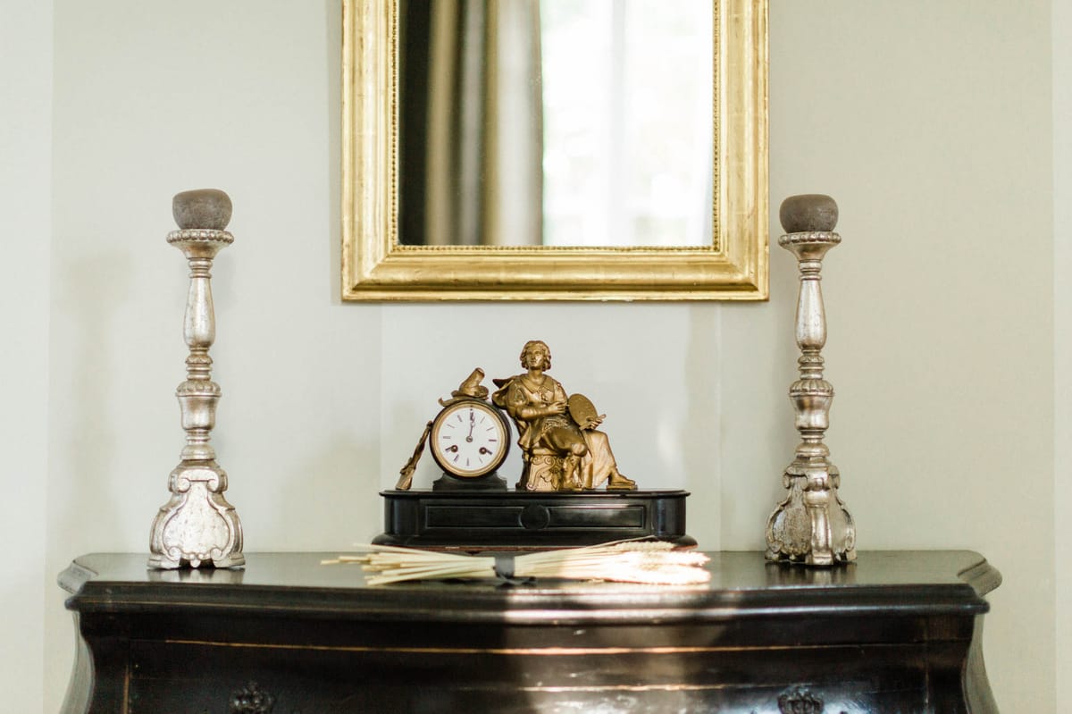 Antique ebonized commode with gilt bronze clock, silver candlesticks, and hand fan below aged gold mirror