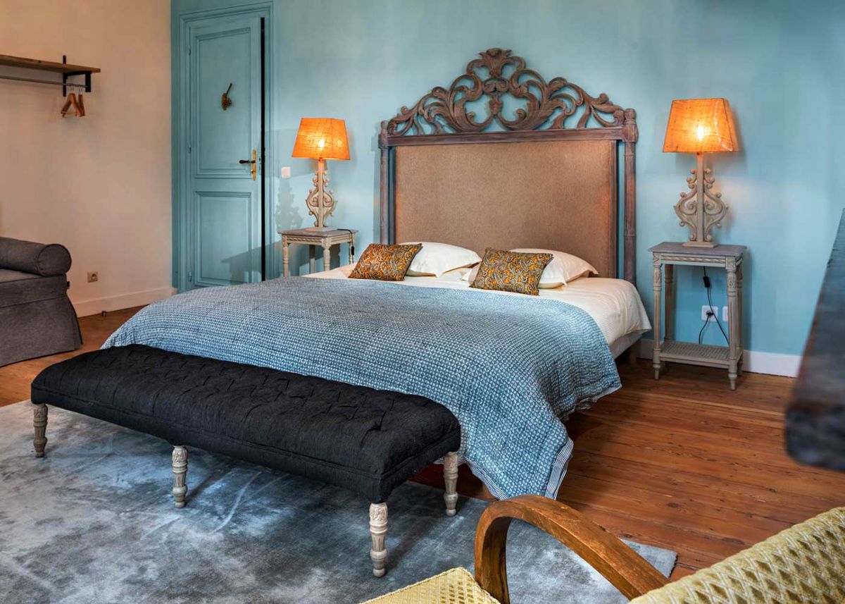 Chateau guest bedroom with baroque carved headboard teal walls and amber table lamps