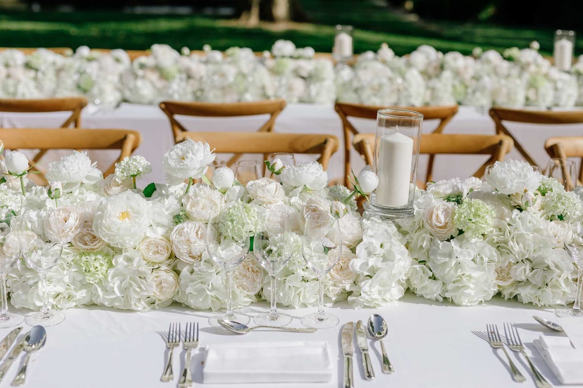 Ivory floral garland of garden roses and peonies along reception table edge with gold Chiavari chairs and glass candles