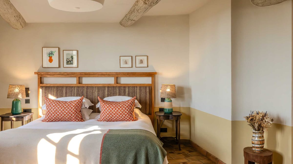 Rustic Provencal bedroom with exposed beams, terracotta floor, woven headboard, and sage green throw