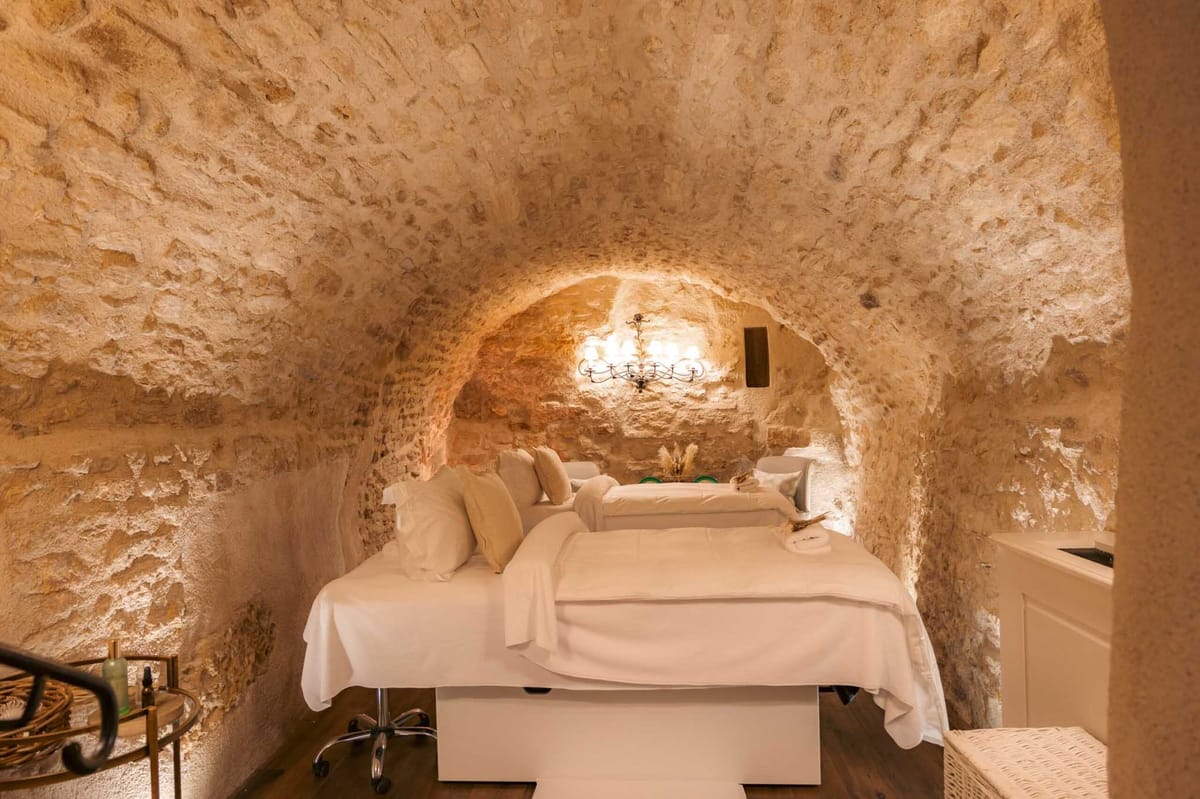 Vaulted stone spa room with two massage tables white linens wrought iron sconce and honey-toned walls