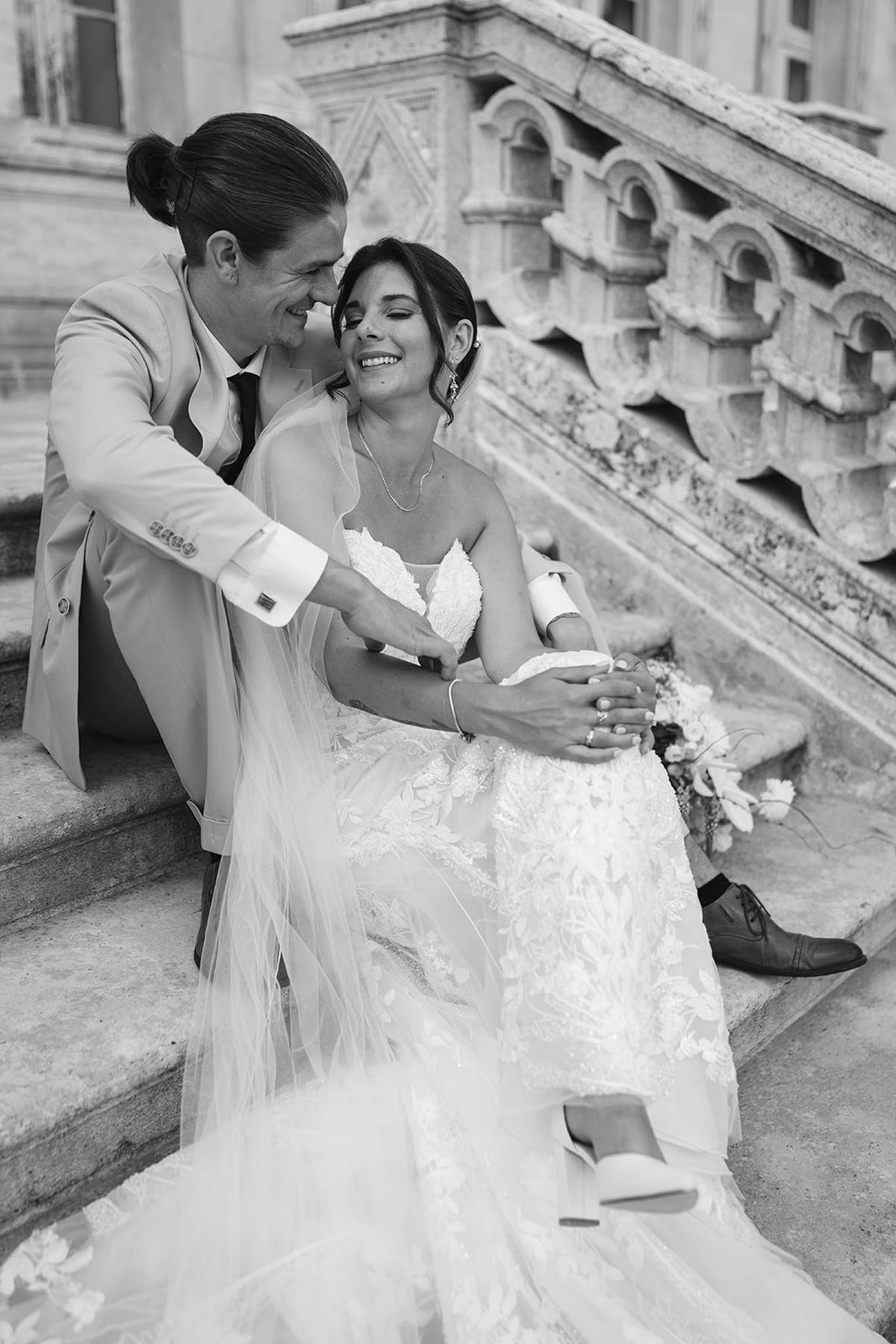 Black-and-white couple laughing on stone steps before ornate Haussmann building facade with arched windows