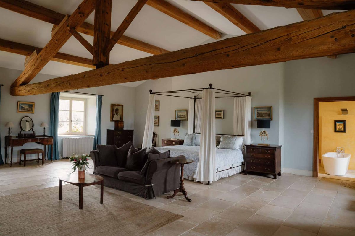 French country bedroom with oak beams wrought-iron four-poster bed mahogany furniture and en-suite freestanding tub