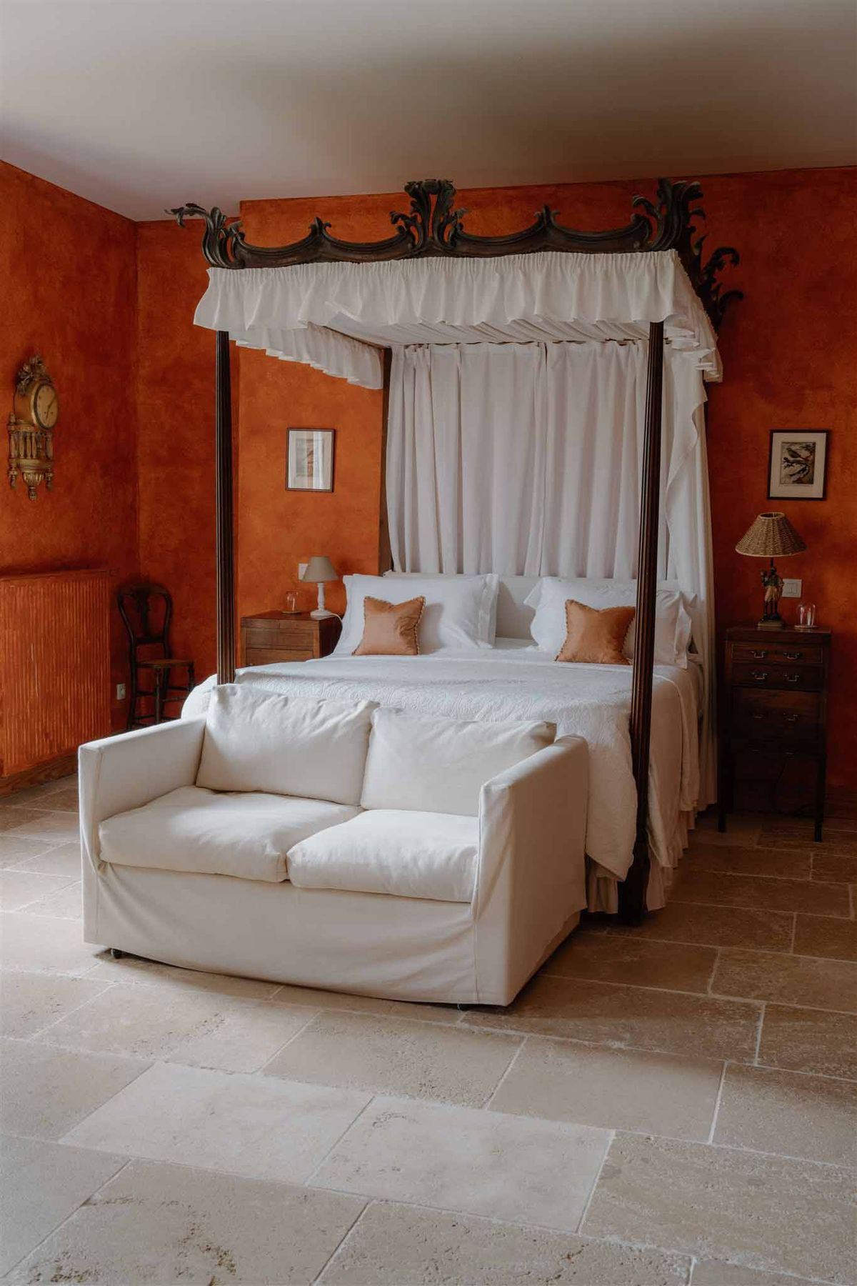 Terracotta-walled bedroom with carved baroque four-poster canopy bed and white linen on limestone floor