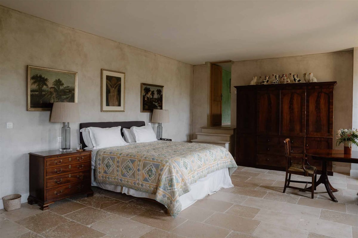 French country guest bedroom with antique walnut furniture, patchwork quilt, and gilt-framed oil paintings