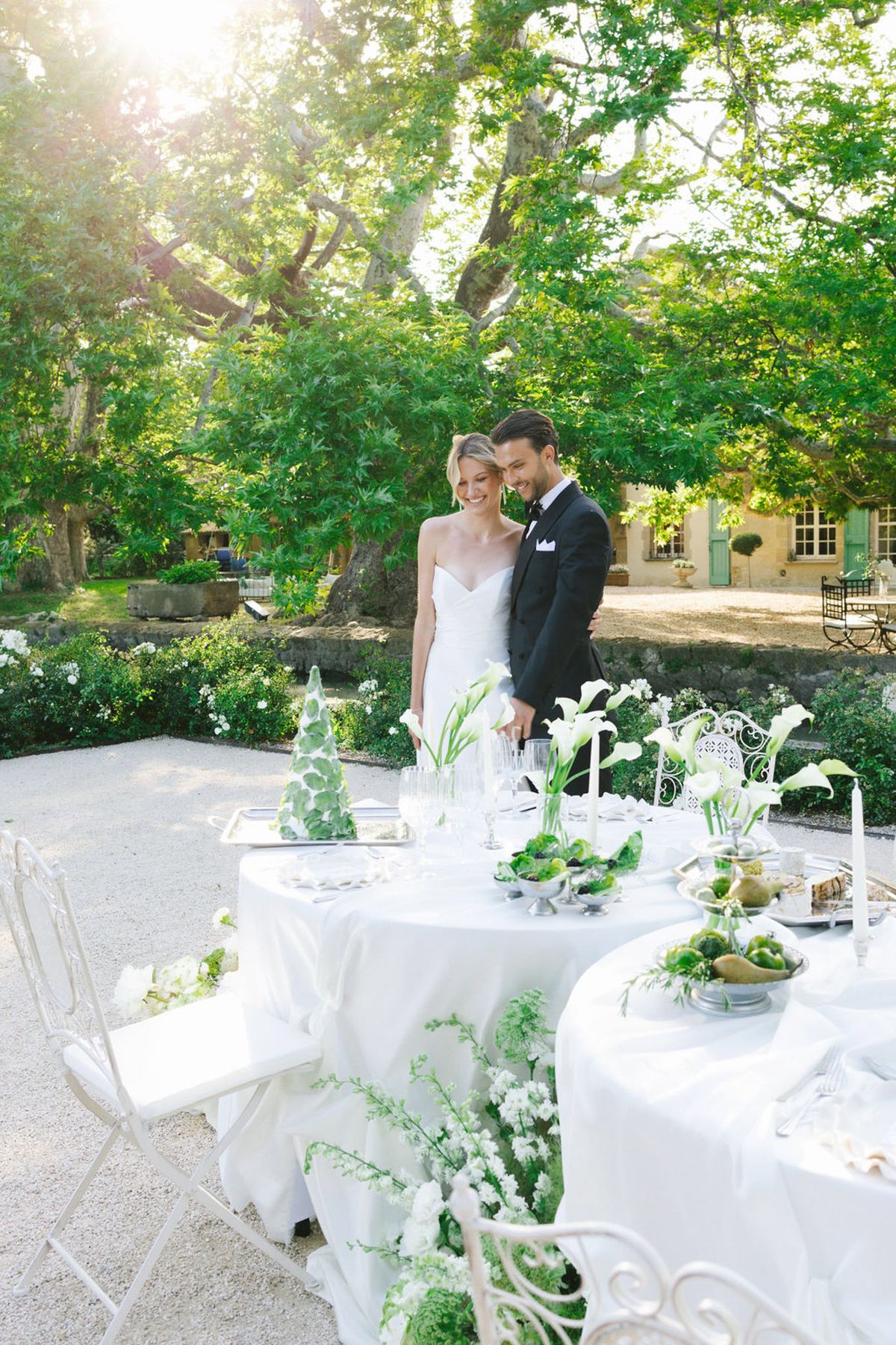 Bride and groom at outdoor reception with round tables, white gardenias, and yellow manor house