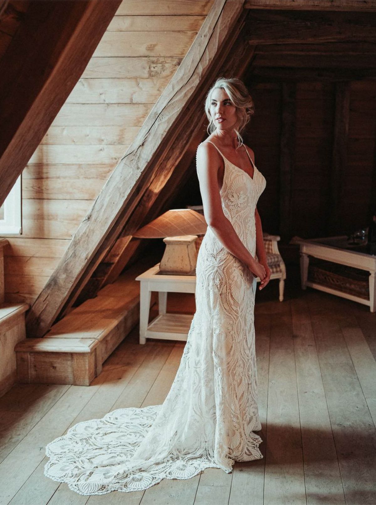 Bride in ivory crochet lace gown with train in rustic attic with exposed wooden beams