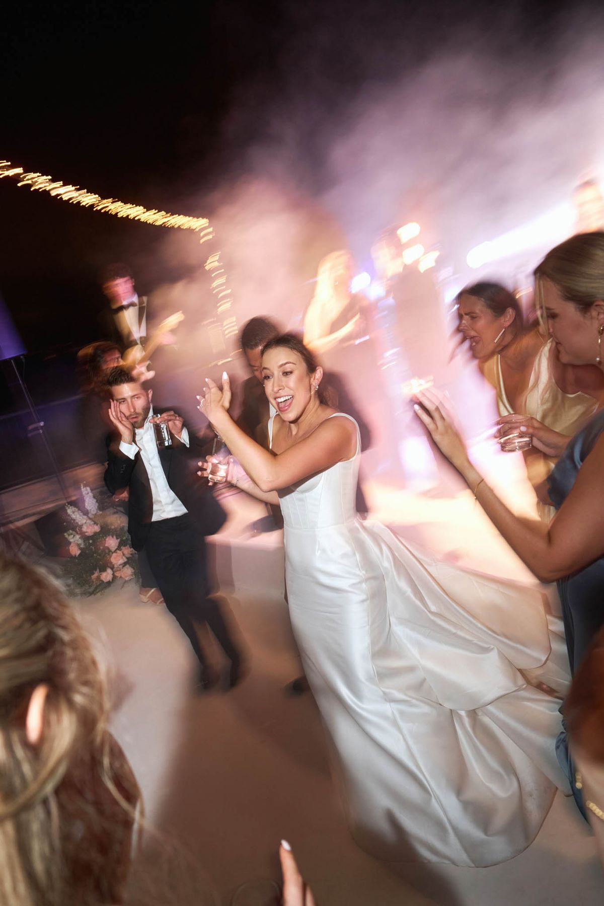 Bride dancing energetically in strapless ballgown with motion blur purple uplights fog and sparkler effects on dance floor