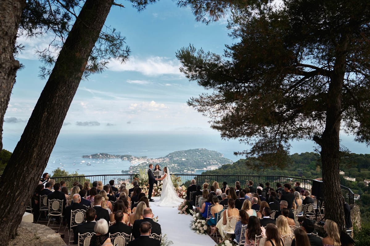 Outdoor wedding ceremony on a coastal terrace overlooking the Mediterranean with gold chairs and floral aisle