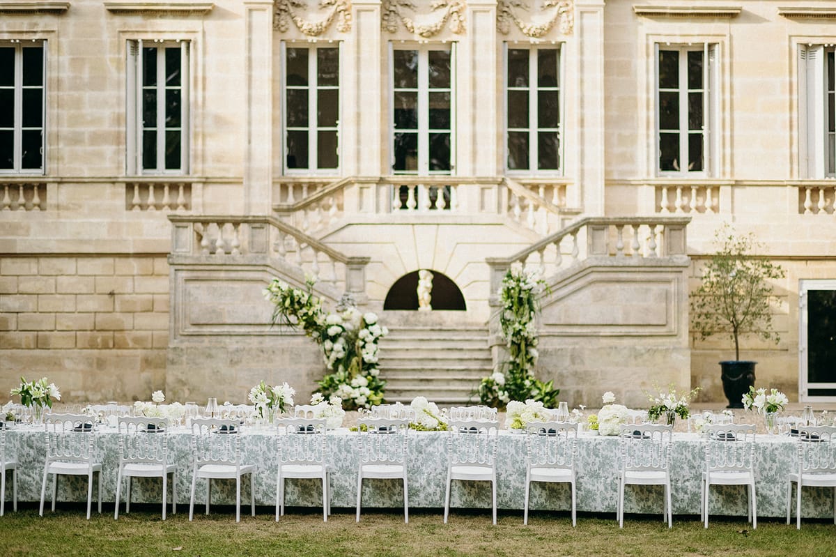 Blue toile table with ghost chairs and white floral staircase arrangements at classical chateau courtyard