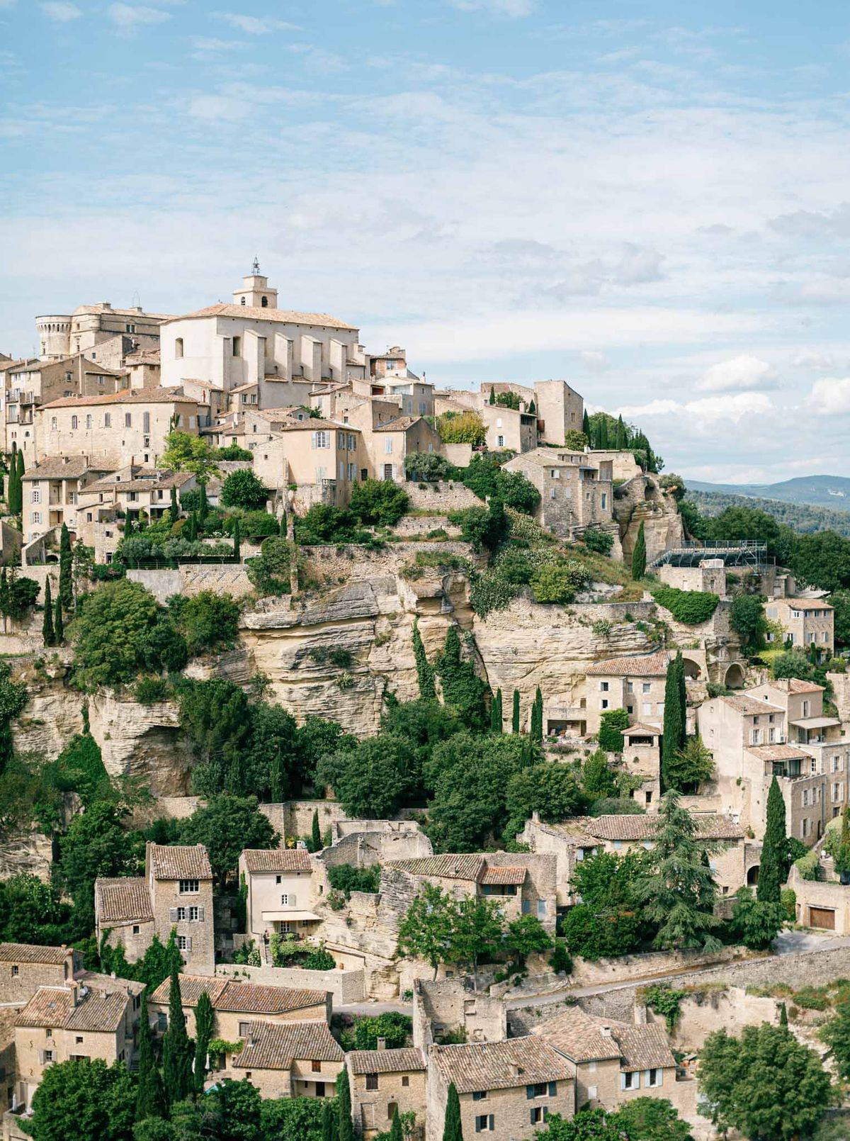 Aerial view of a hilltop Provencal village with stone buildings and church bell tower against distant mountains