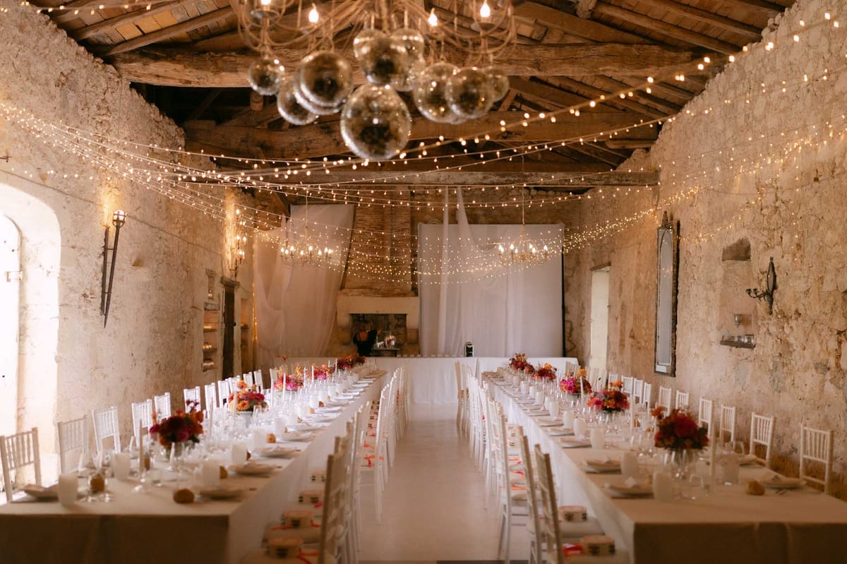 Stone barn reception with disco balls, fairy lights, hot pink and orange centrepieces, and white chiavari chairs