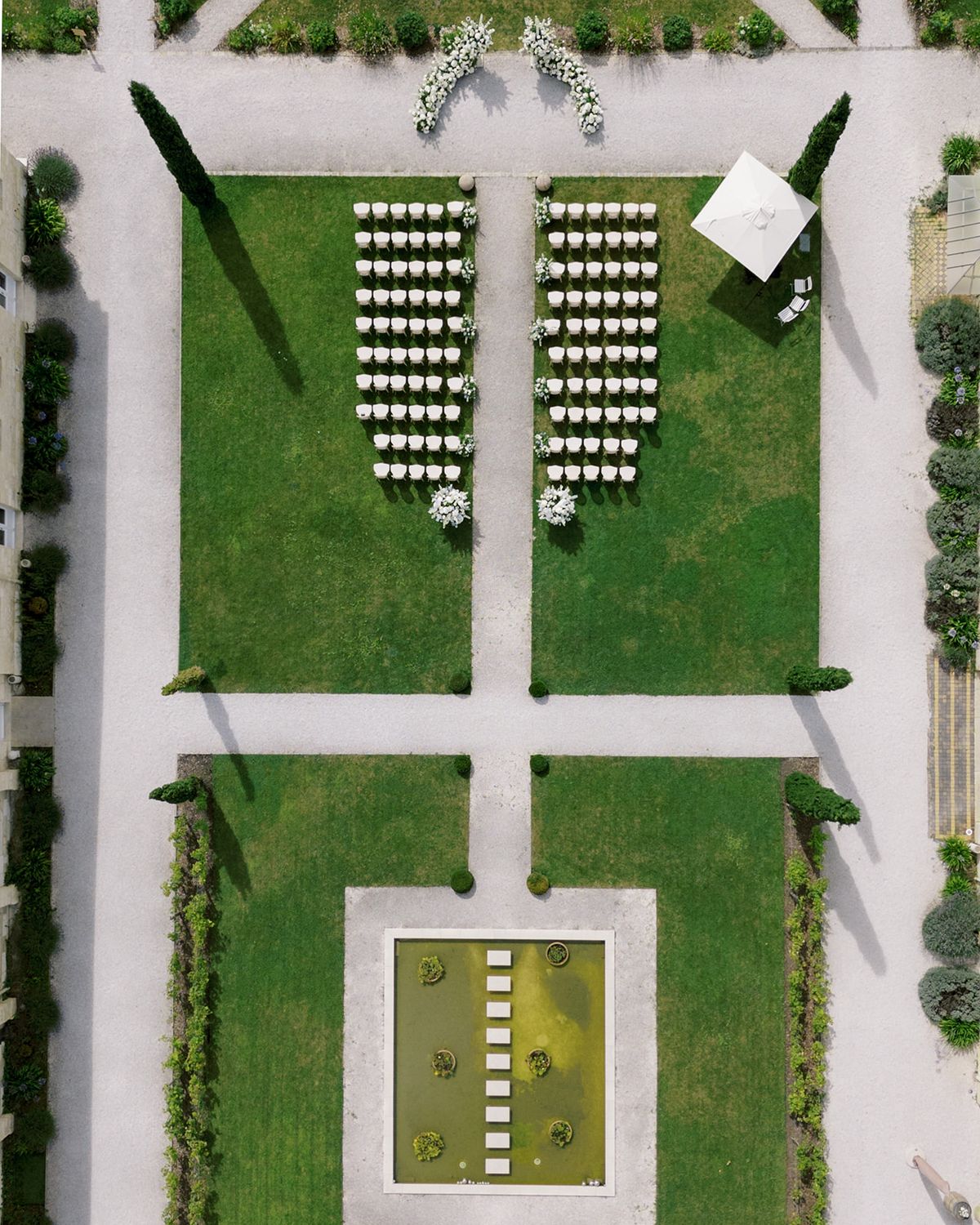 Aerial view of formal garden ceremony setup with white Chiavari chairs arranged symmetrically on lawn with boxwood borders