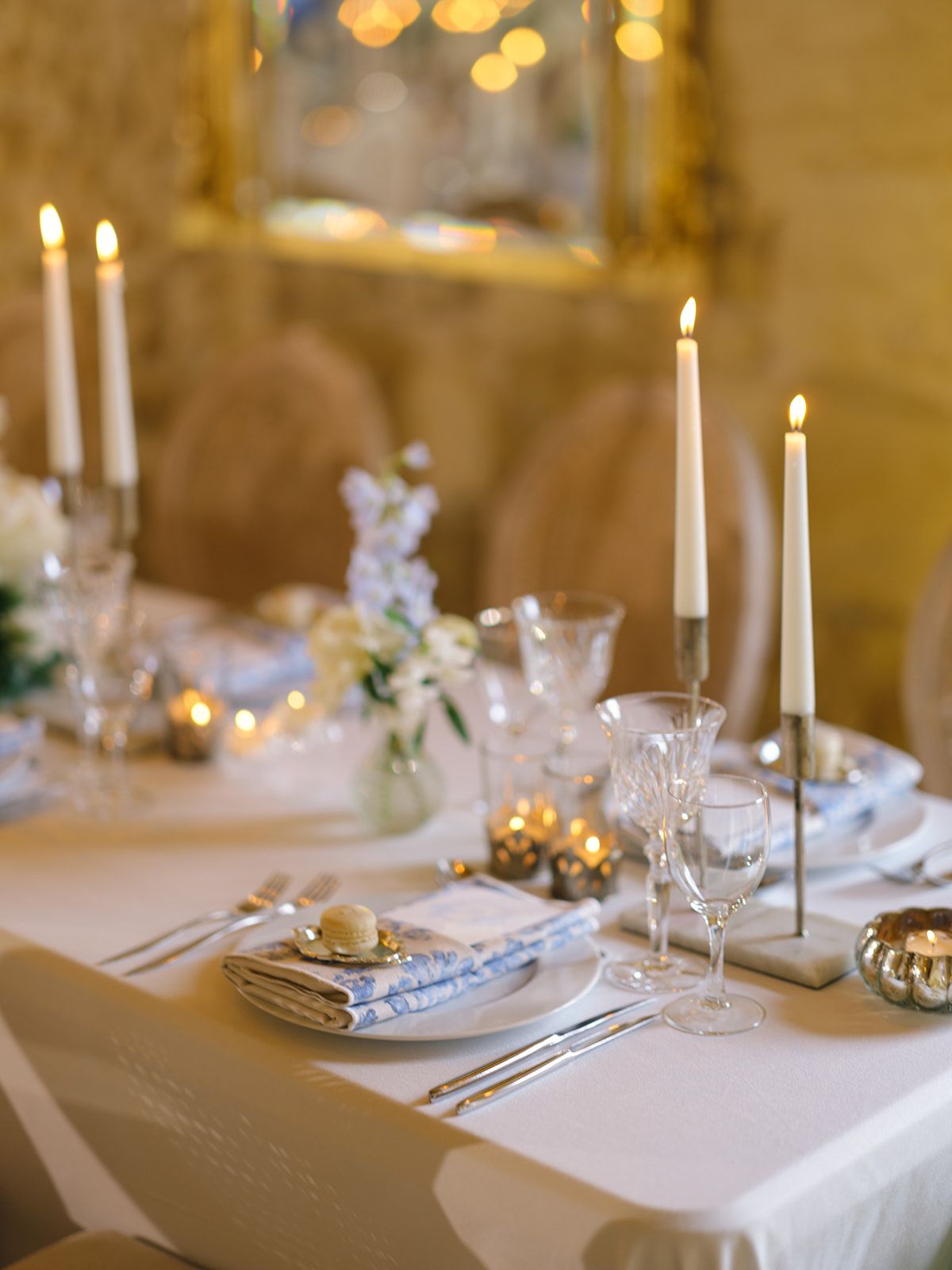 Formal table setting with blue striped napkins, gold candlesticks, white flowers and crystal glassware on white linen