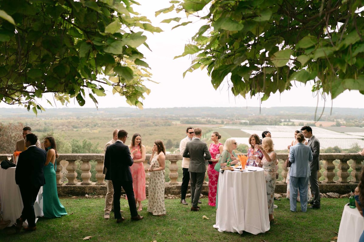 Guests mingling on a chateau terrace during cocktail hour with rolling countryside and vineyard views behind