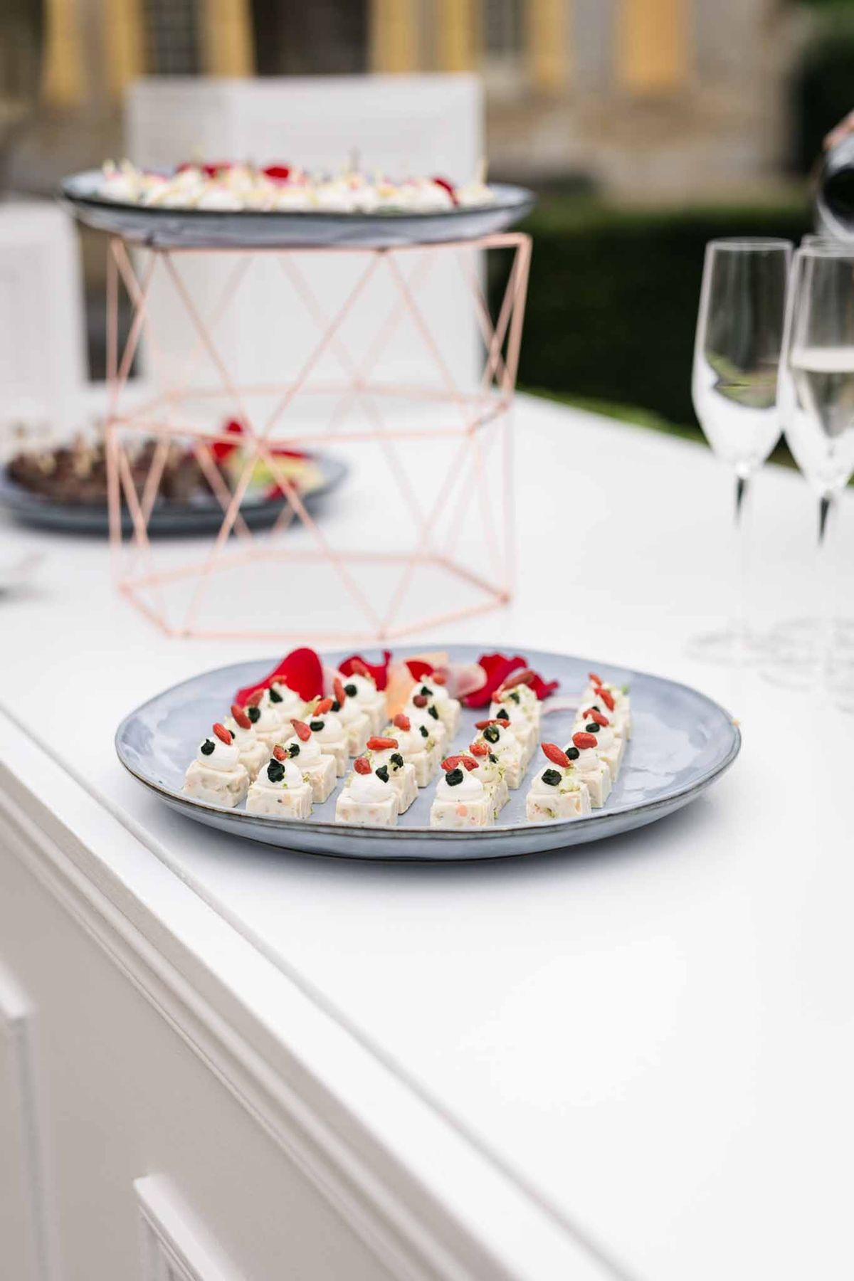 Close-up of cream petit fours with strawberry and caviar on slate-blue plate with rose-gold wire centerpiece