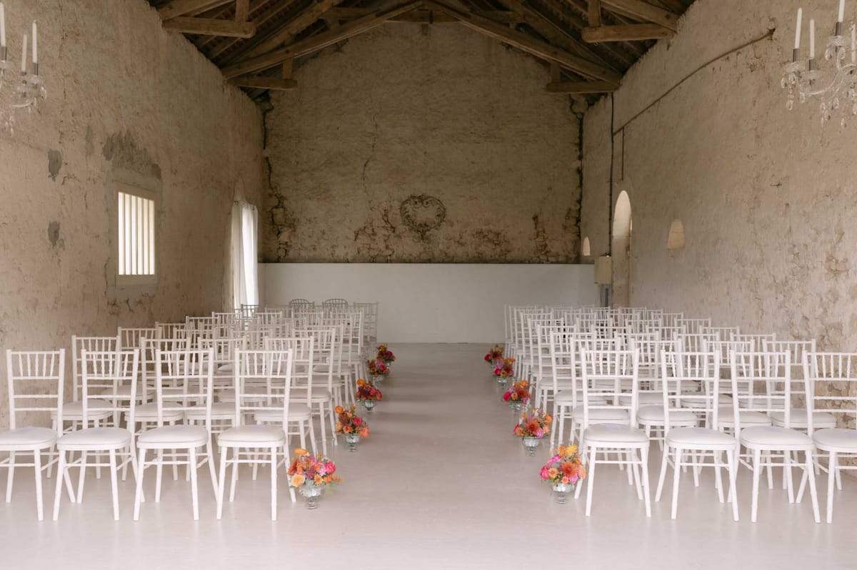 Rustic barn ceremony setup with white chiavari chairs and orange and pink floral aisle arrangements