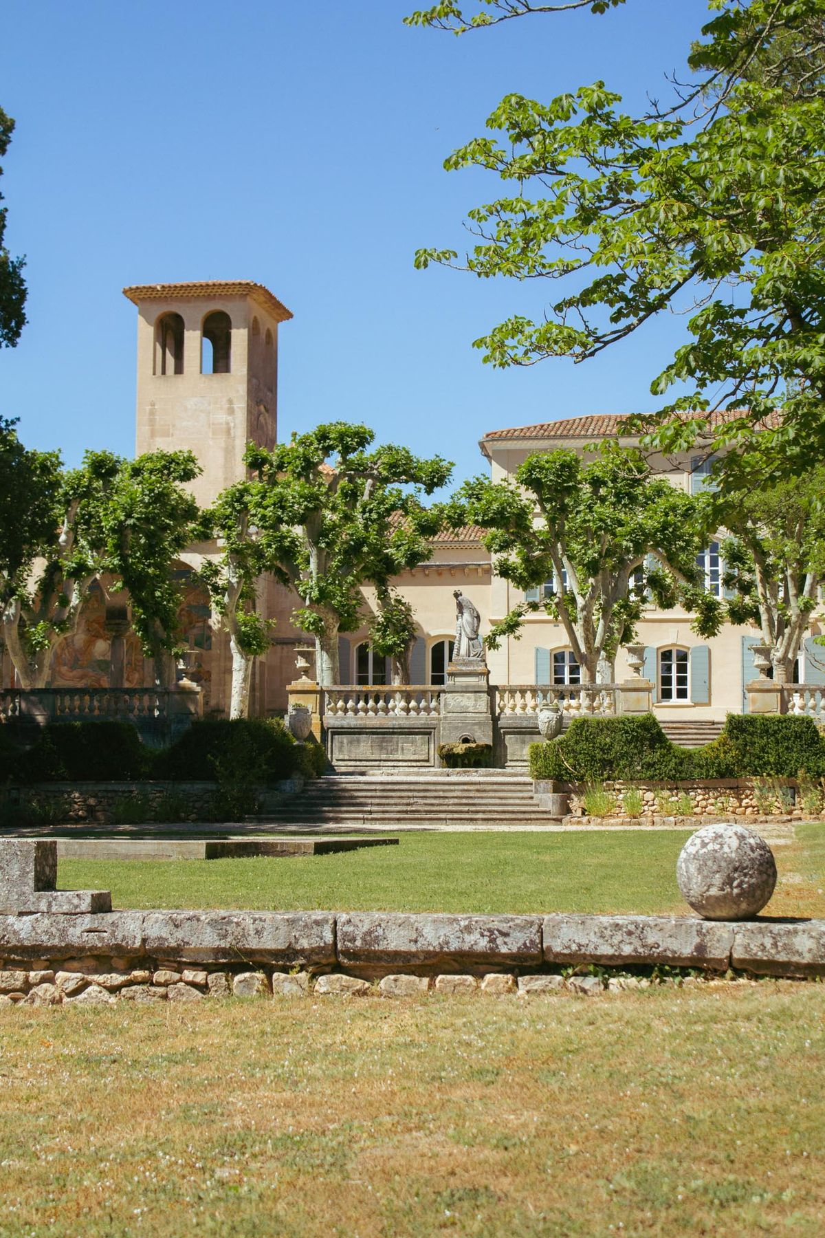 French estate with honey-toned stone, bell tower, balustrade terrace, classical statue, and pollarded plane trees