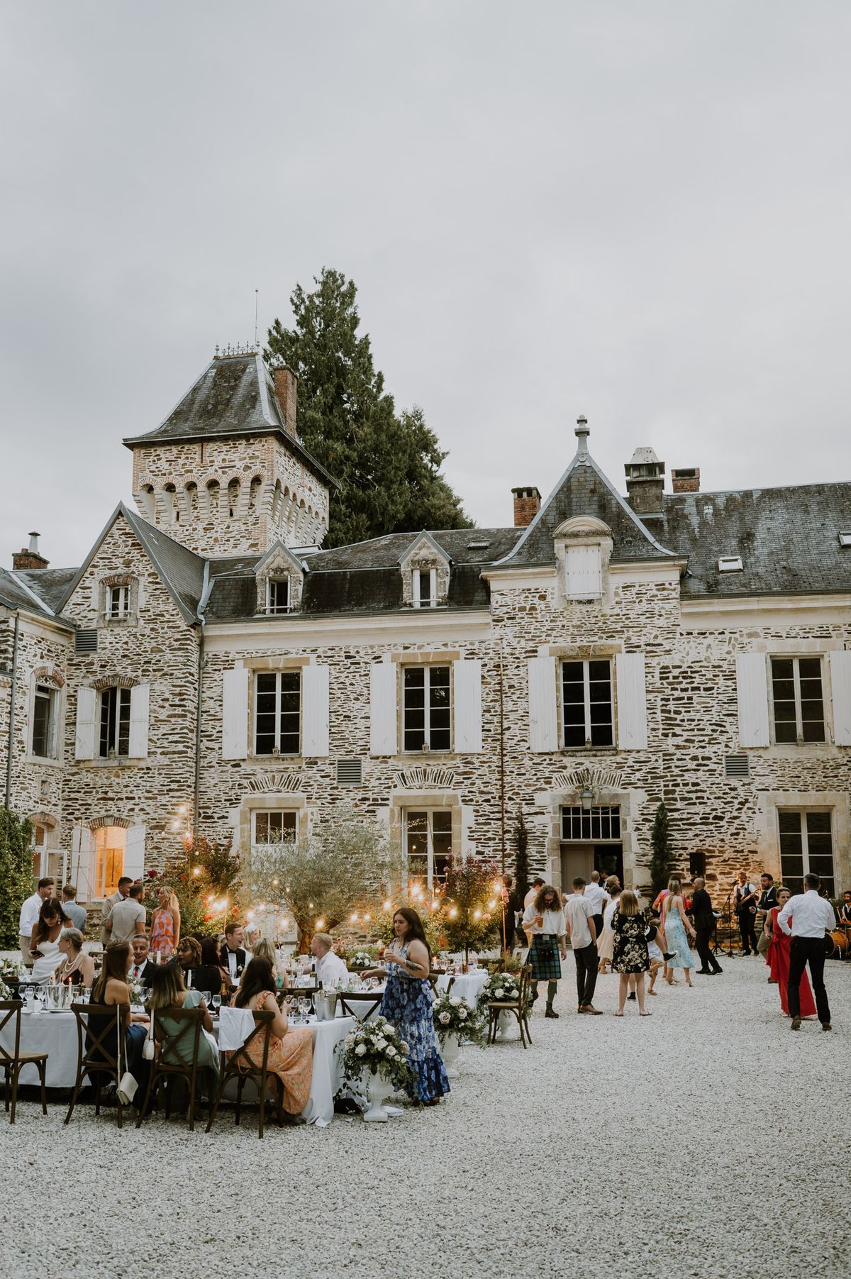Evening courtyard reception at chateau with festoon lights through olive trees and 40 guests
