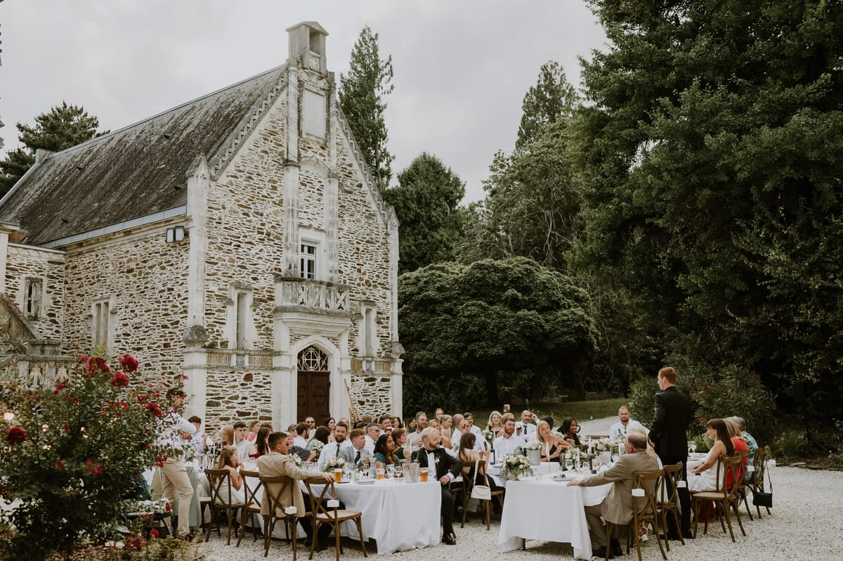 Outdoor reception dinner with 50-60 guests at round tables in front of a Gothic-style French stone manor