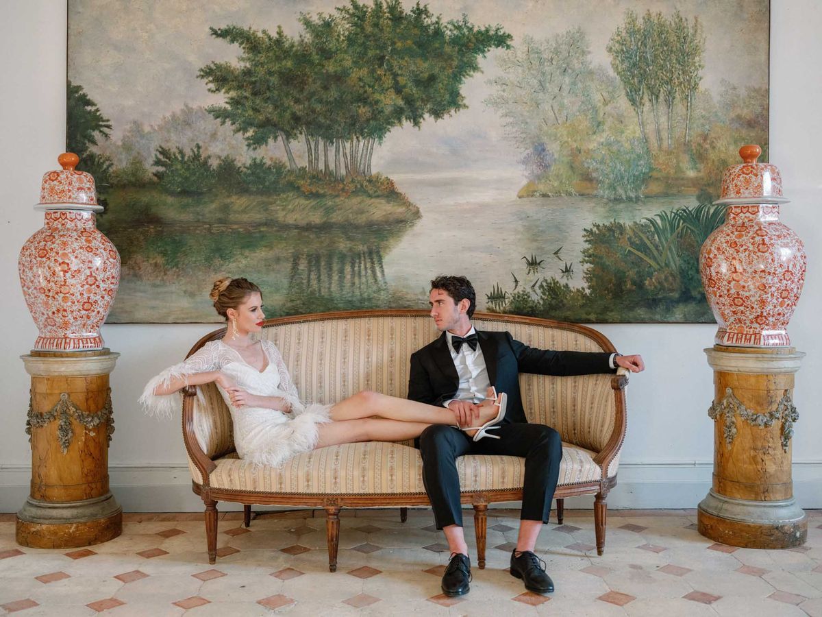Couple posed on Louis XVI sofa with bride in feather-trimmed dress and groom in tuxedo