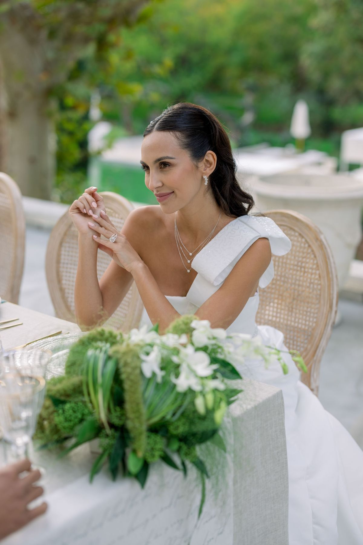 Bride admiring engagement ring at outdoor reception table with green and white floral arrangement