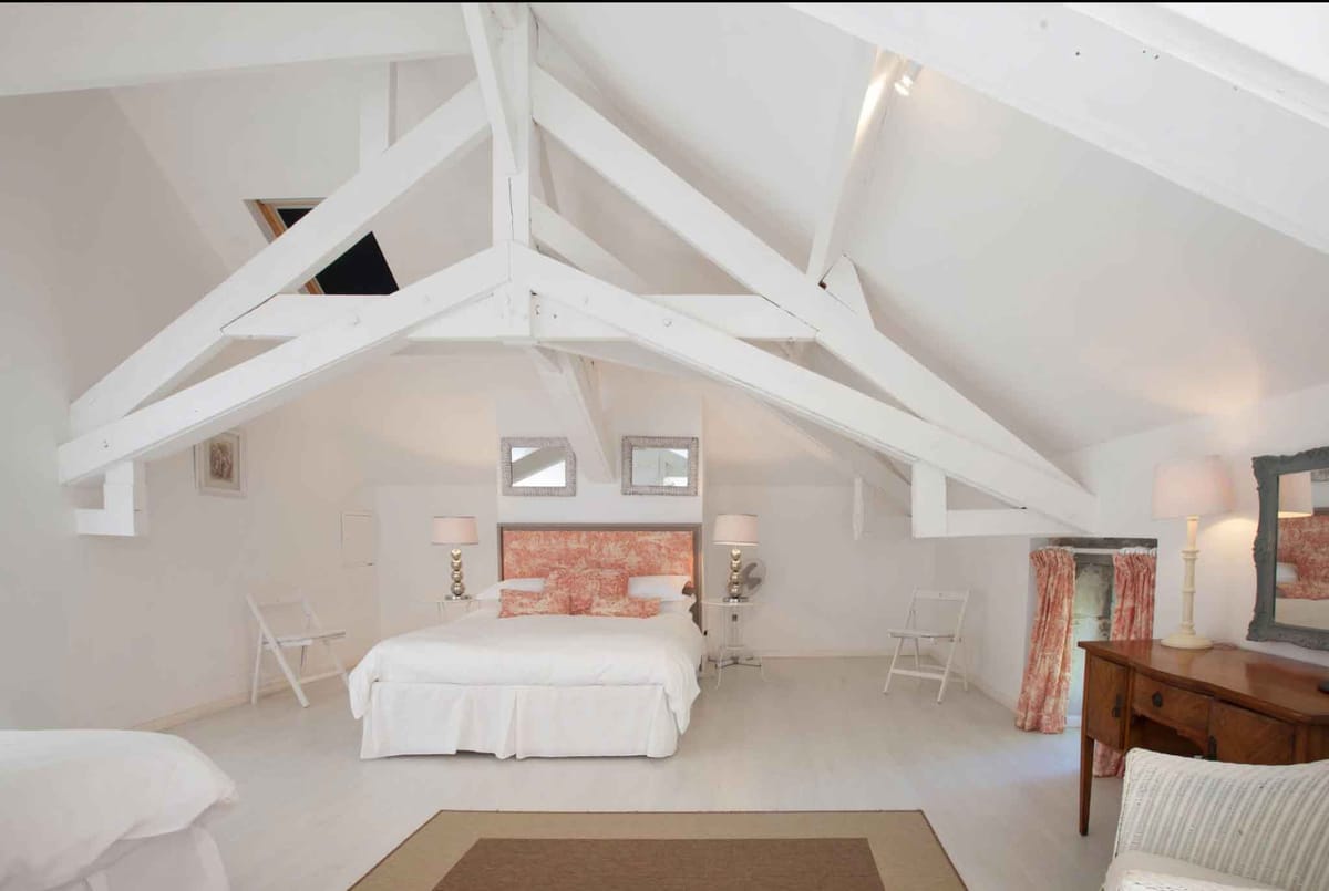 Bedroom suite with coral-red toile de Jouy headboard, exposed white beams, and wicker mirrors