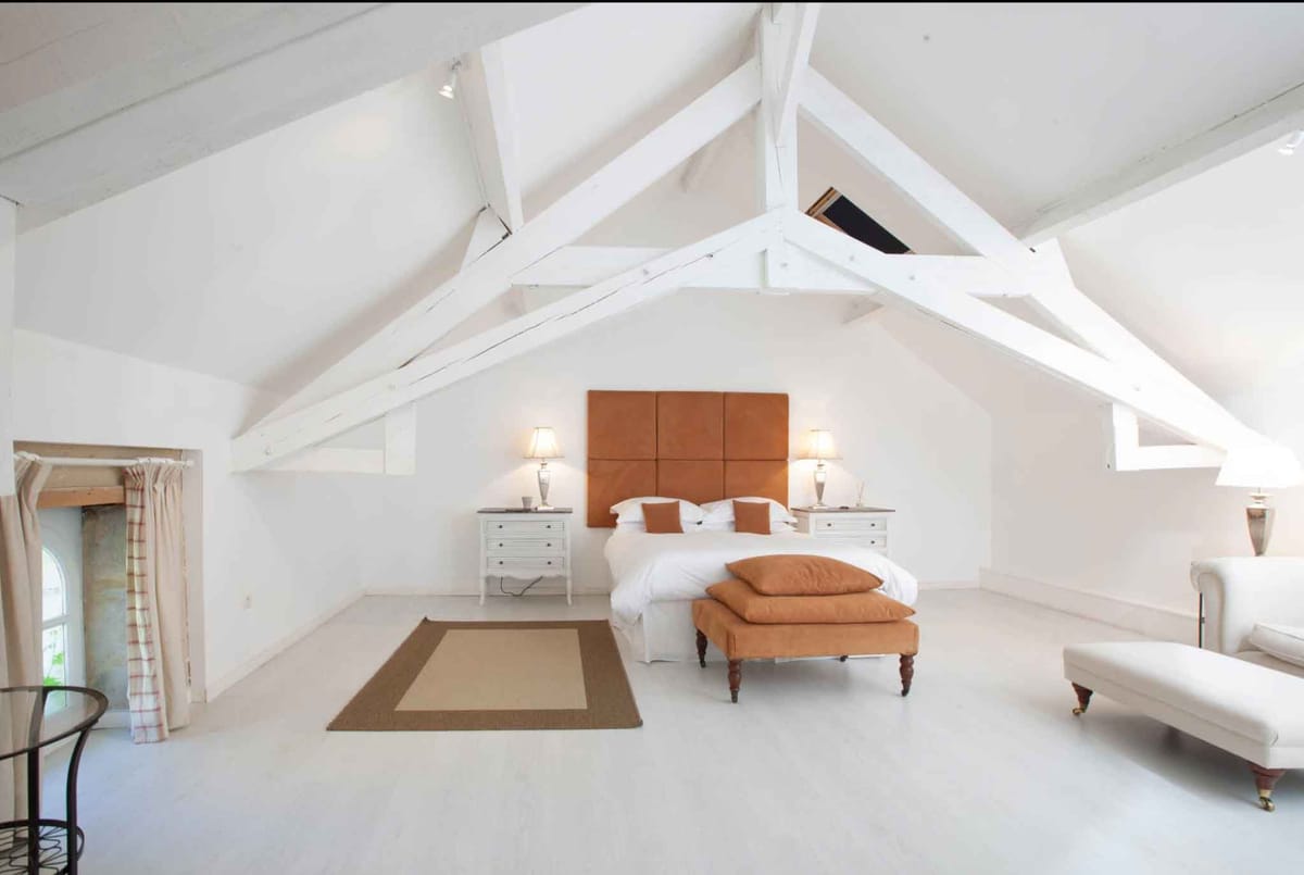 Attic bedroom suite with exposed timber beams, burnt orange headboard, and skylight above