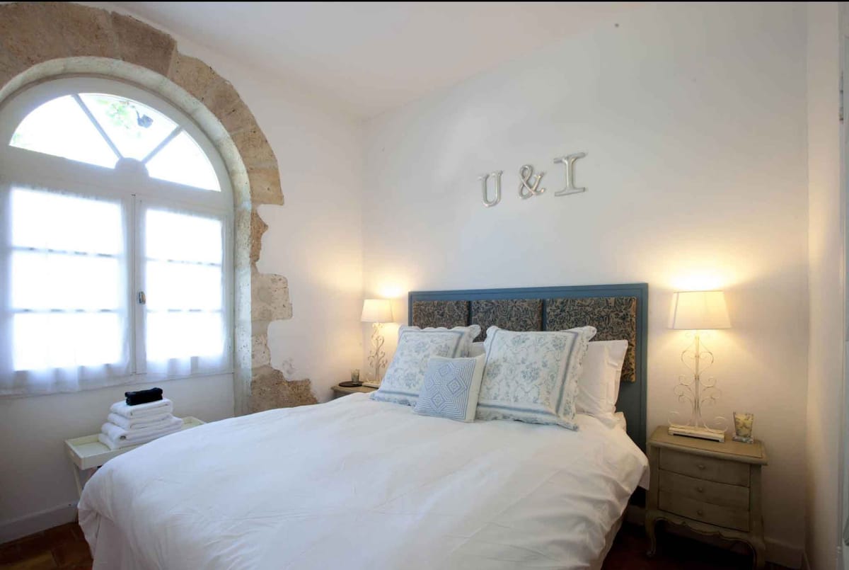 Bridal suite bedroom with blue upholstered headboard, floral cushions, and arched stone window shutters